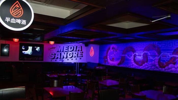 Interior del bar y sala de cerveza Media Sangre con luces de neón, mesas oscuras y arte de dragón en Araiza Calafia