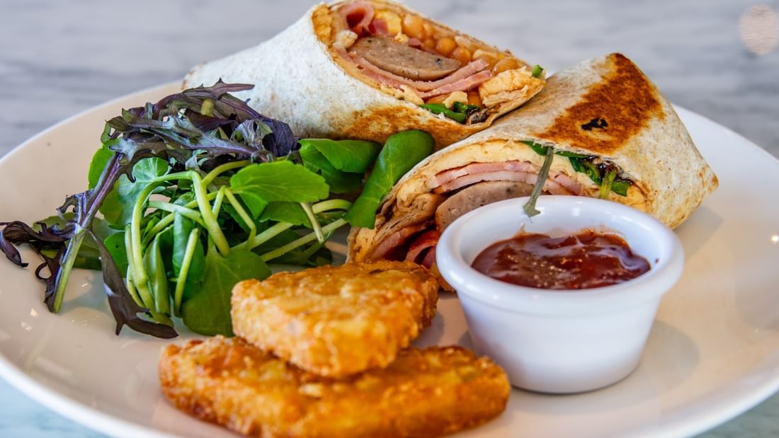 Plate with two sandwiches, a small salad, two fried items, and a cup of ketchup.