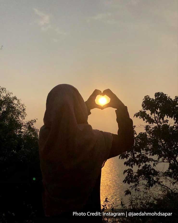 a girl doing a hand heart pose around the sun