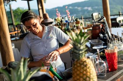 A woman standing at the bar counter & making a cocktail in Gaviota's Bar at Villas Sol Beach Resort
