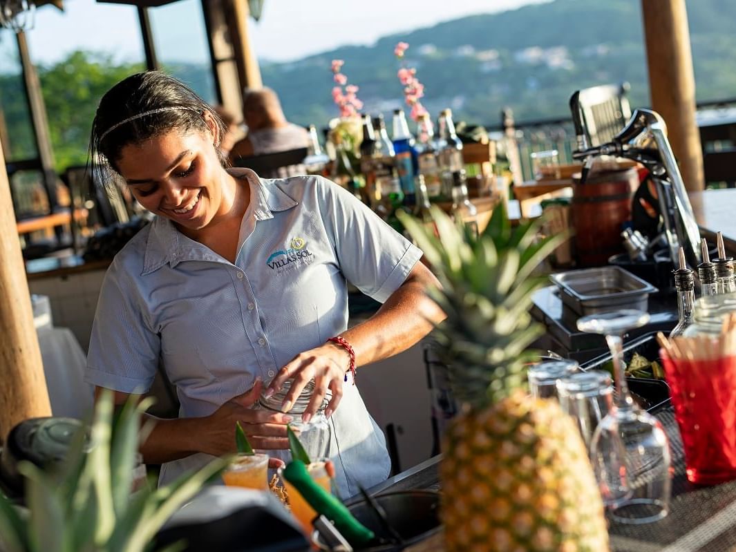 A woman standing at the bar counter & making a cocktail in Gaviota's Bar at Villas Sol Beach Resort