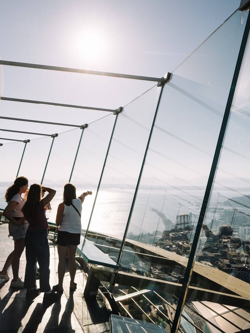 People looking at a city view by glass walls under the bright sun in a tower near Warwick Seattle