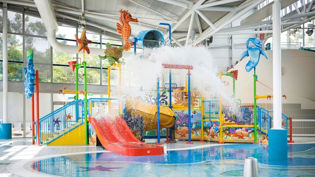 Indoor water play area featuring slides and a large splash zone at Aquatic Centre near Novotel Sydney Olympic Park