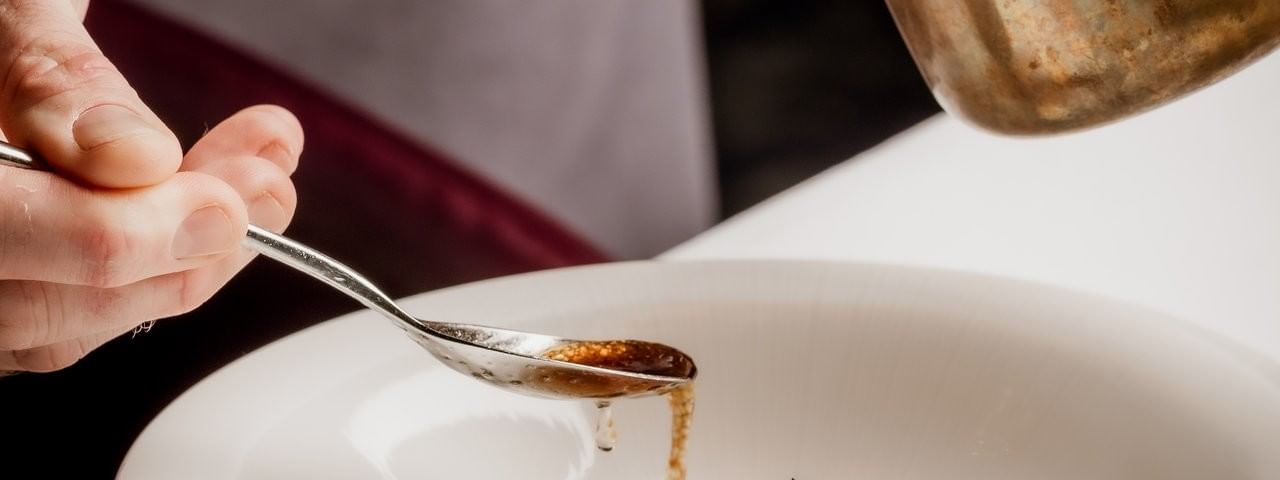 Chef using a spoon by a copper pot to plate a raw fish dish under sauce at The Capital Hotel, Apartments and Townhouse
