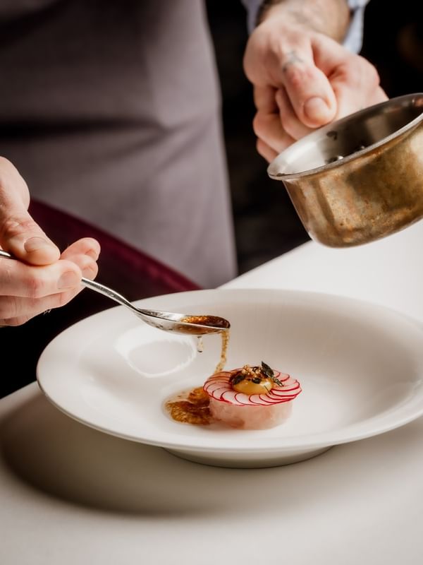 Chef using a spoon by a copper pot to plate a raw fish dish under sauce at The Capital Hotel, Apartments and Townhouse