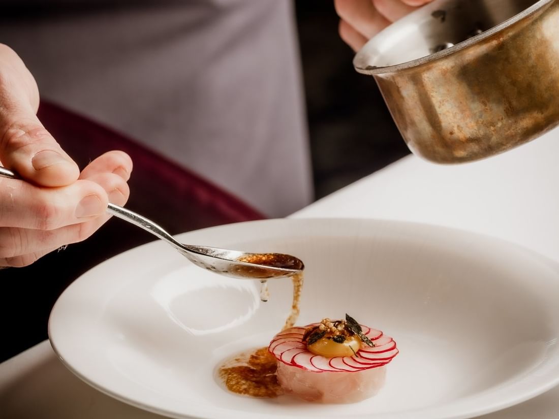 Chef using a spoon by a copper pot to plate a raw fish dish under sauce at The Capital Hotel, Apartments and Townhouse