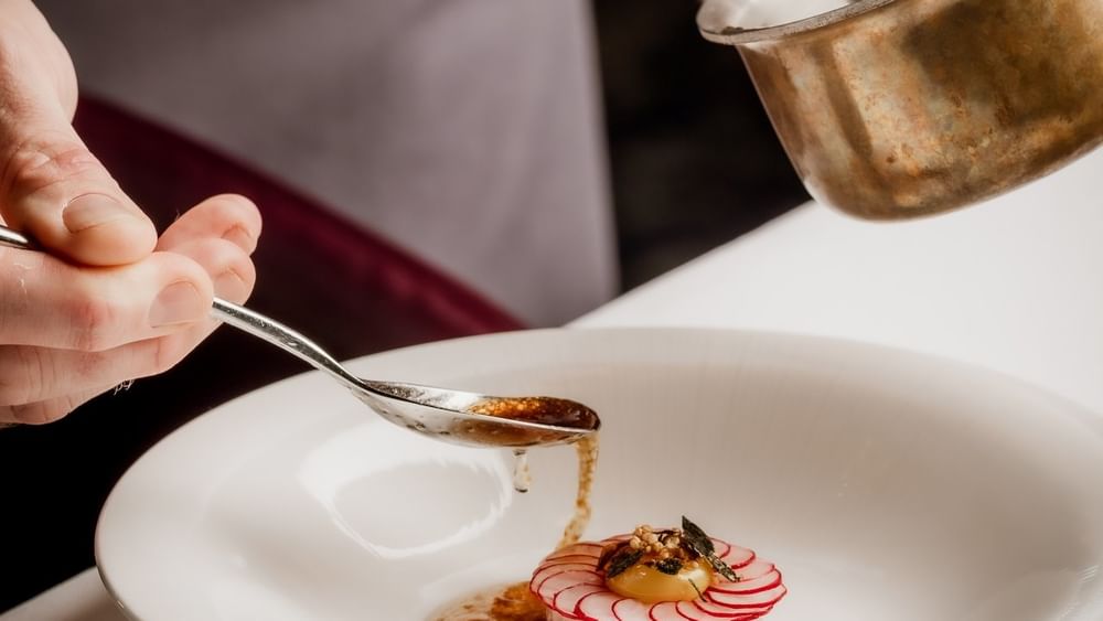 Chef using a spoon by a copper pot to plate a raw fish dish under sauce at The Capital Hotel, Apartments and Townhouse