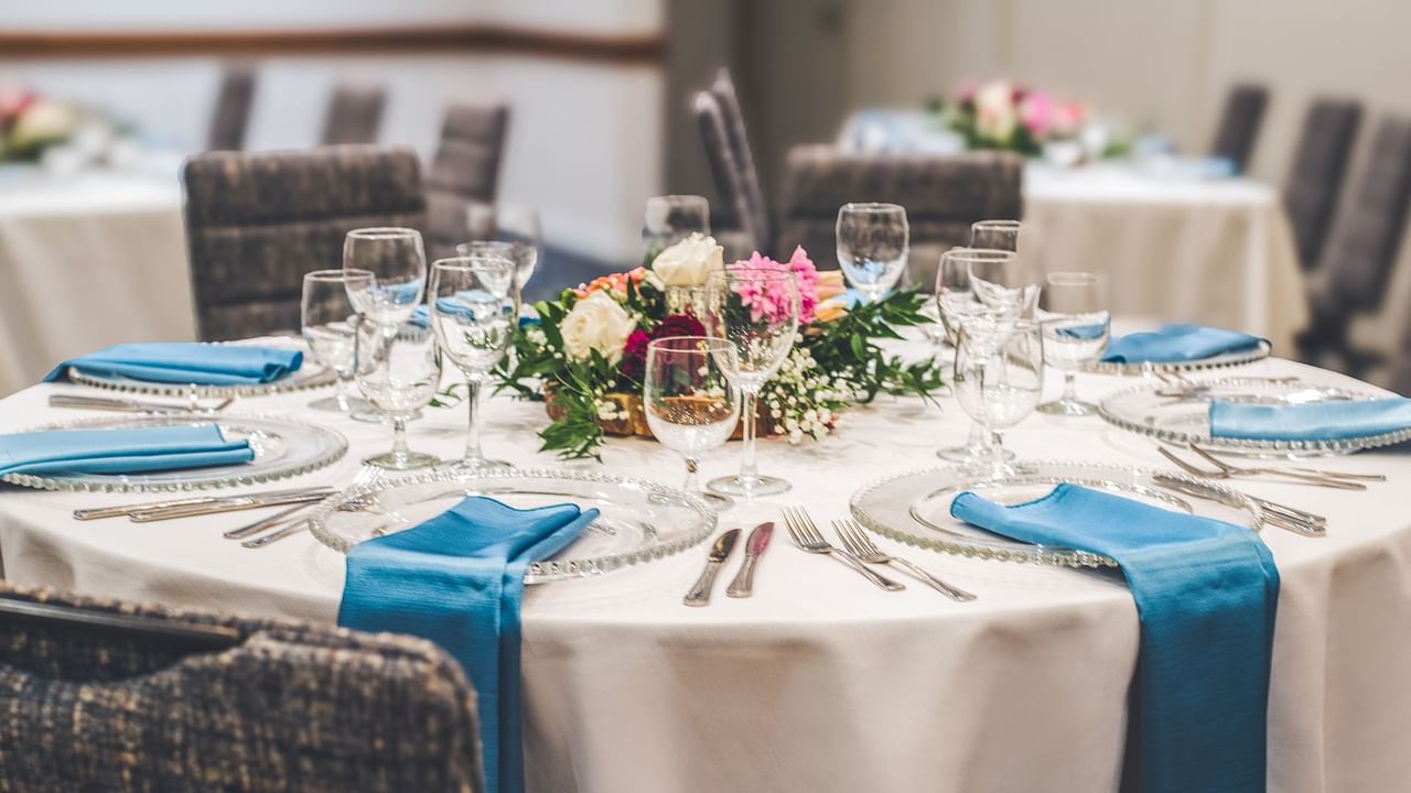 A set table with white tablecloth, blue napkins, clear glasses, silverware, and a floral centerpiece.
