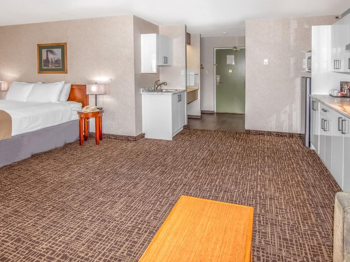 A hotel room with a bed, carpeted floor, wooden table, kitchenette, and a couch.
