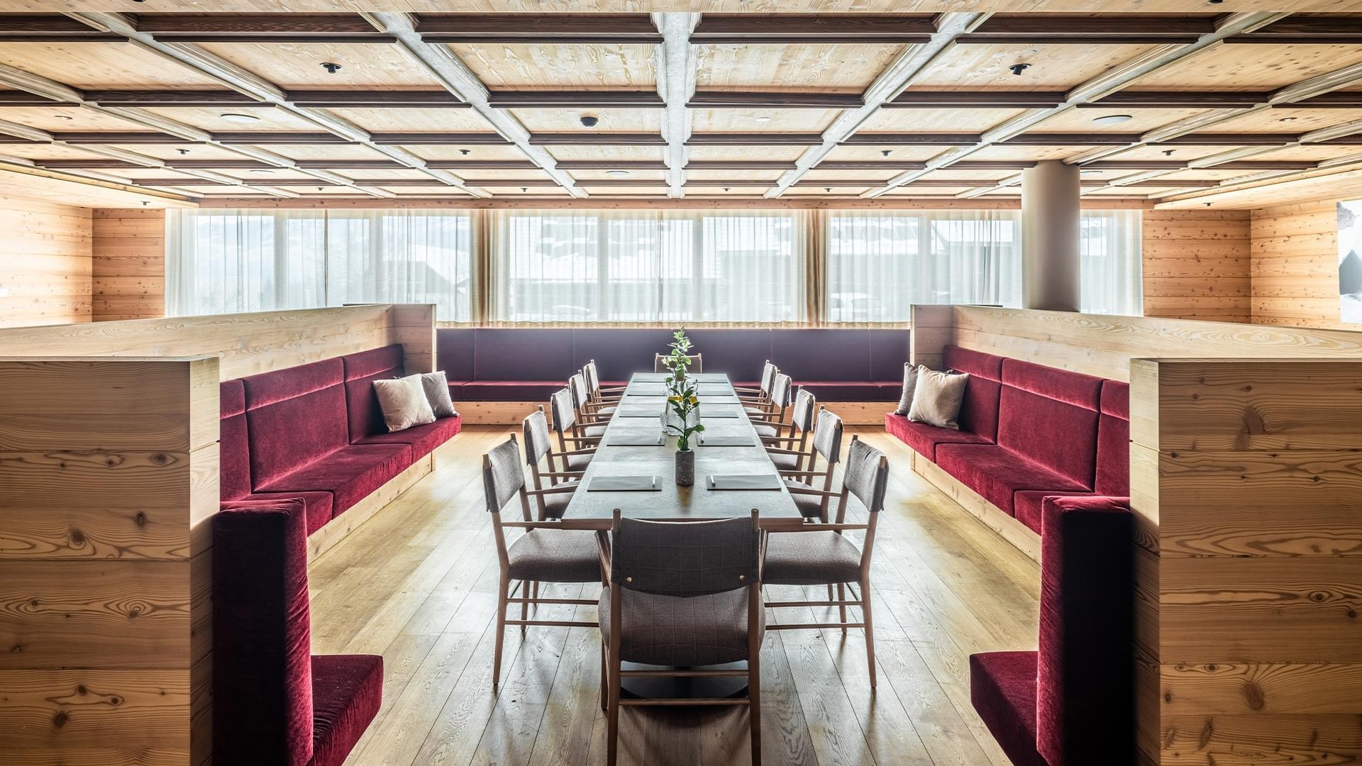 Meeting room with wooden panels, long table, chairs and red couches at Falkensteiner Hotel Kronplatz