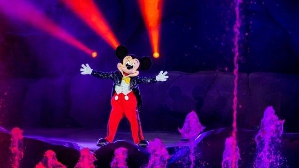 Mickey Mouse wearing a black and red tuxedo standing onstage with his arms outstretched during a performance of Fantasmic at Hollywood Studios.