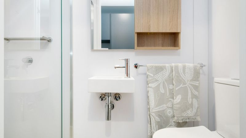 Bathroom with white sink, mirror, wooden cabinet, glass shower enclosure, and white toilet.