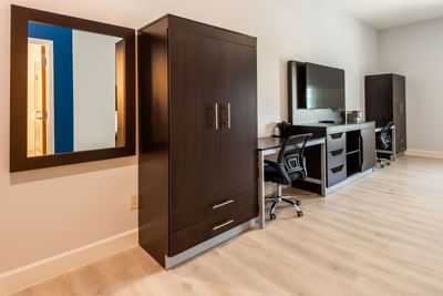 Cozy room with dark wood wardrobe, work desk, wall-mounted TV, and light wooden flooring at The J Hotel