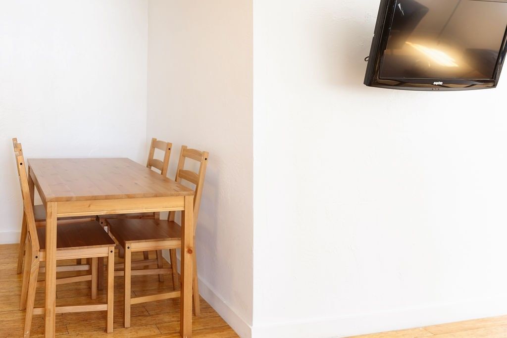 A small dining area with a table and chairs, and a TV mounted on the wall.