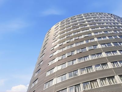 Tall modern building with many windows under a blue sky, part of Student Living Auckland - Beach.