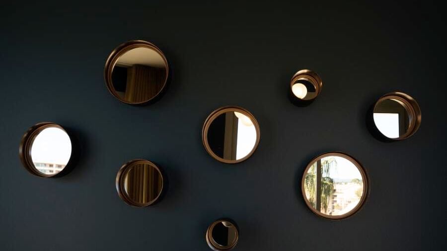 Plusieurs miroirs ronds de tailles variées accrochés sur un mur sombre.