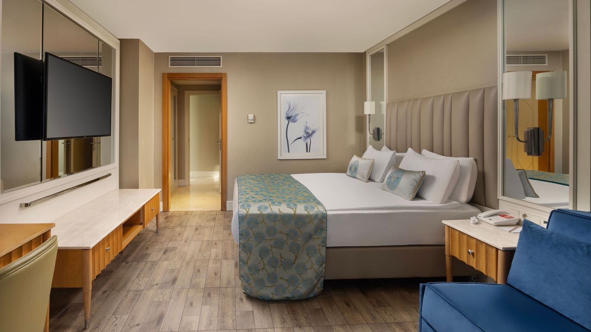 Wall-mounted TV with wooden cabinet facing bed with decorative pillows in Junior Suite at Titanic Deluxe Lara