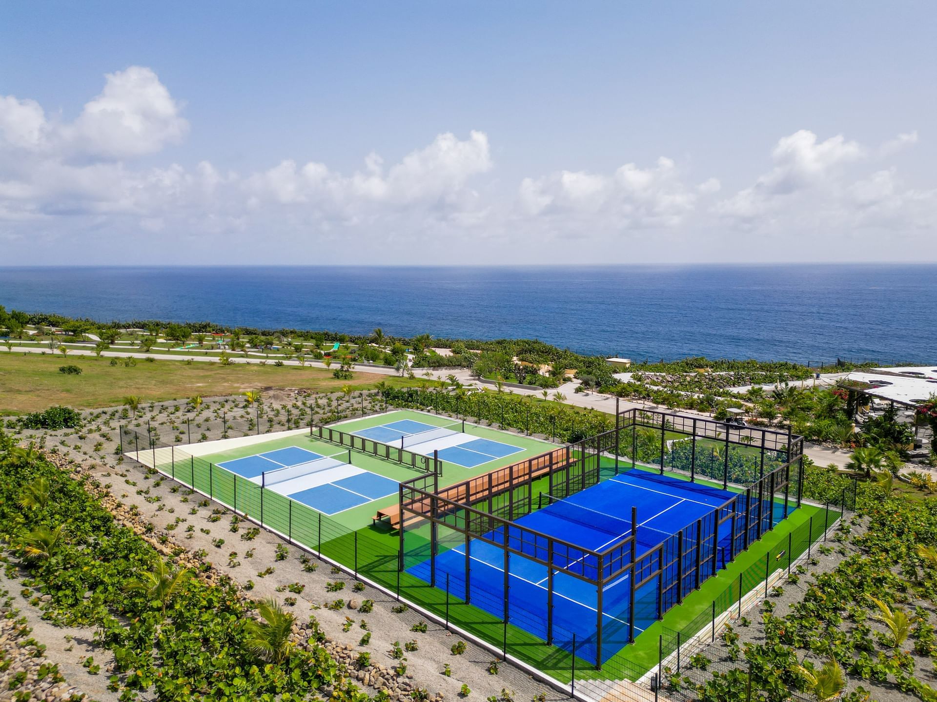 Panoramic view of colorful tennis courts and a padel court by the ocean, surrounded by lush greenery near Golden Rock Resort