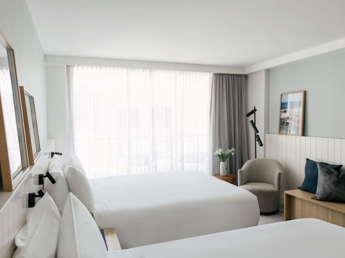 Atrium Twin at Elysium Manly with a grey armchair by a wooden bench under framed art near floor-to-ceiling sheer curtains