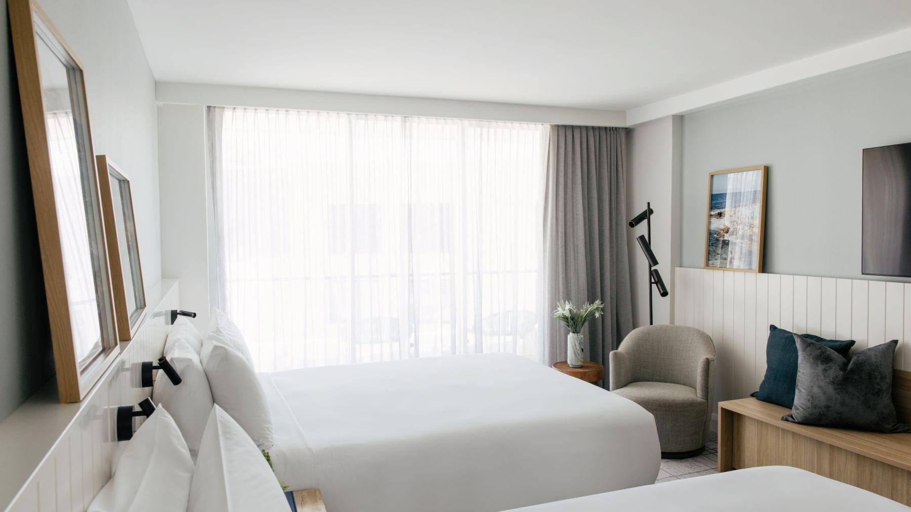 Atrium Twin at Elysium Manly with a grey armchair by a wooden bench under framed art near floor-to-ceiling sheer curtains
