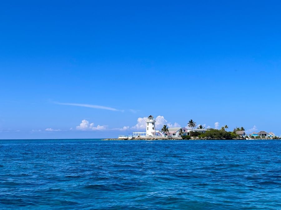 White lighthouse by small buildings on a green island under a vast blue sky near Warwick Paradise Island Bahamas