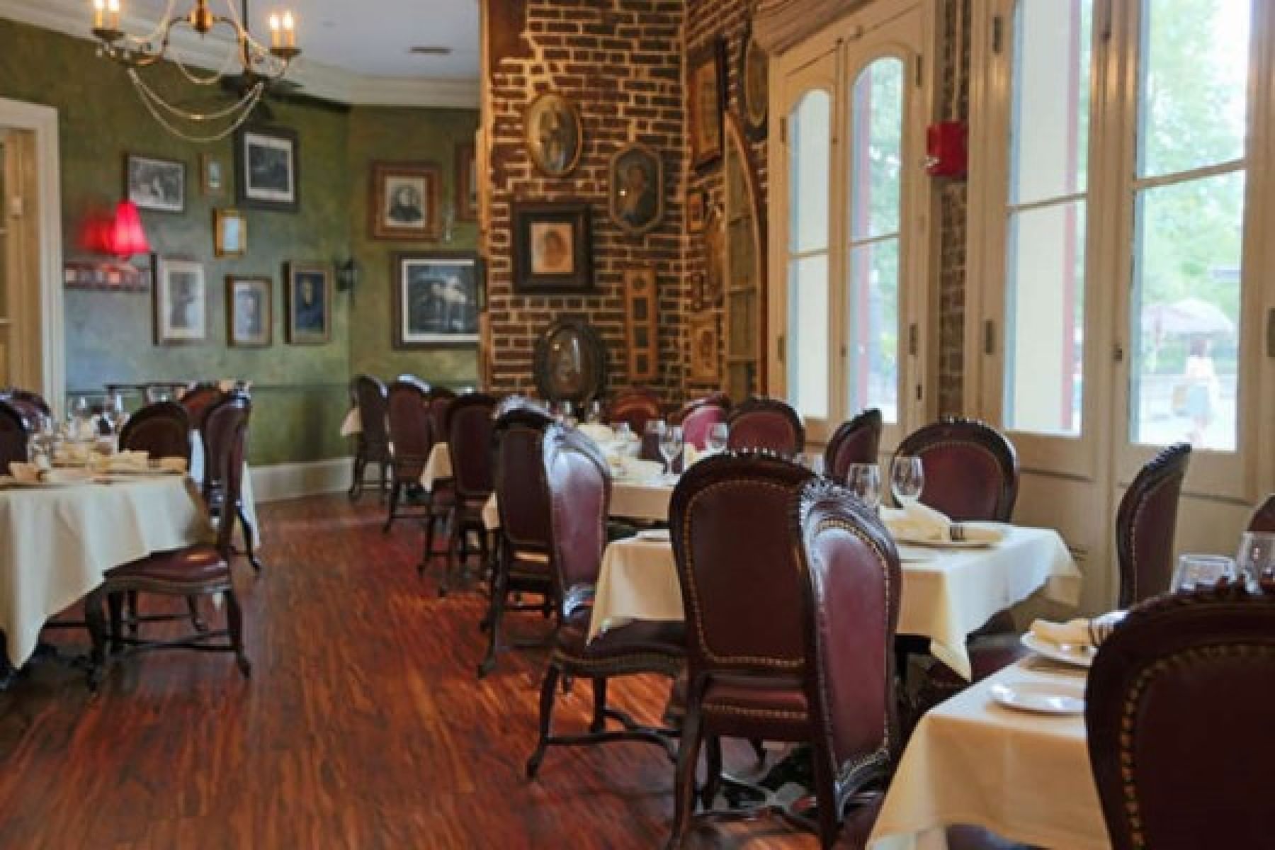 A dining room with a brick wall, dark wood floor, and leather chairs