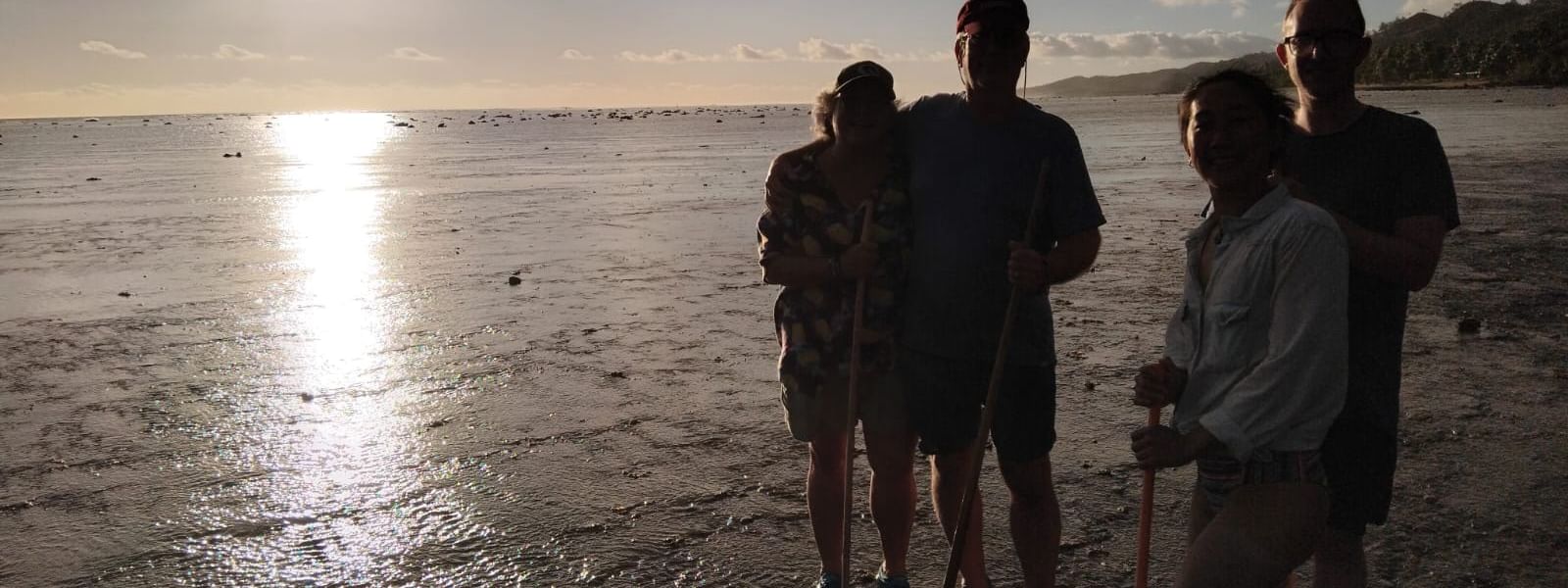 Four people with walking sticks at sunset on a beach reef at Tambua Sands Beach Resort in Sigatoka