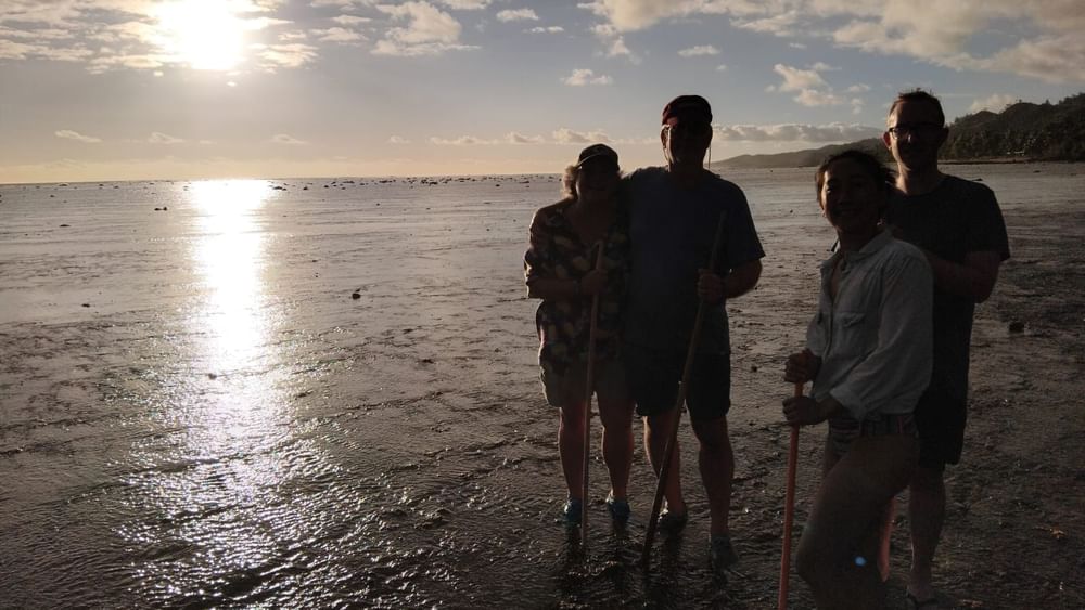 Four people with walking sticks at sunset on a beach reef at Tambua Sands Beach Resort in Sigatoka.