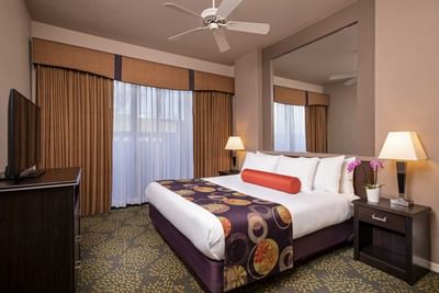 Hotel room with white bedding, decorative runner, ceiling fan, and brown curtains at London Bridge Resort