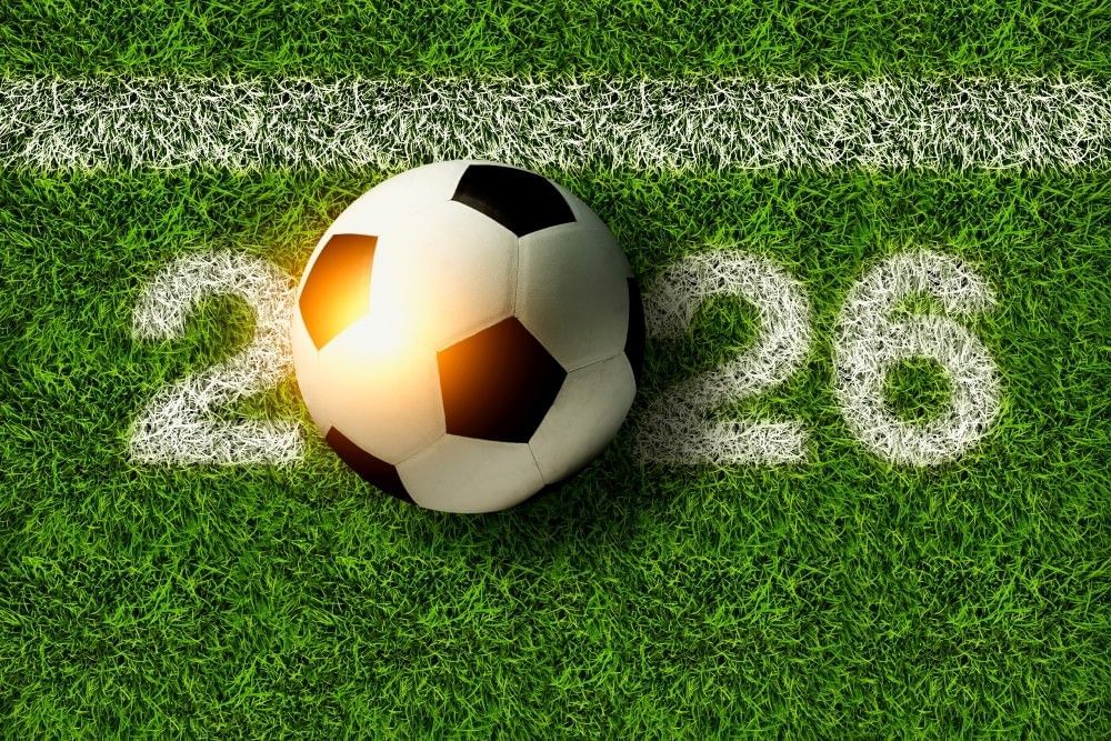 A soccer ball on green turf with white painted boundary lines, and the numbers 2026 printed across it.