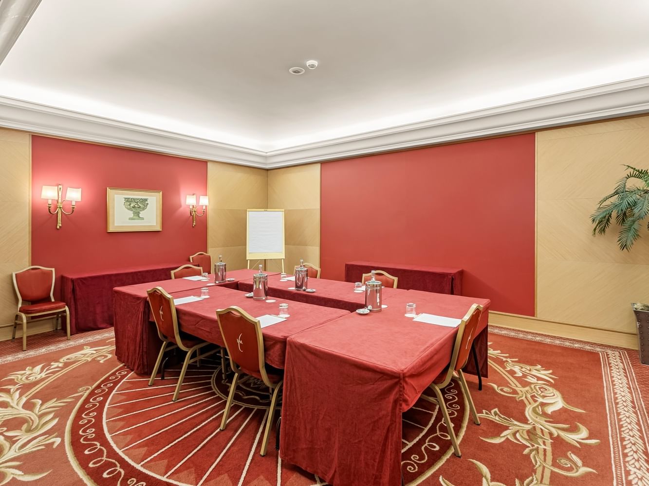 Sala de reuniones con mesas y sillas, paredes rojas y beige, y una planta en la esquina.