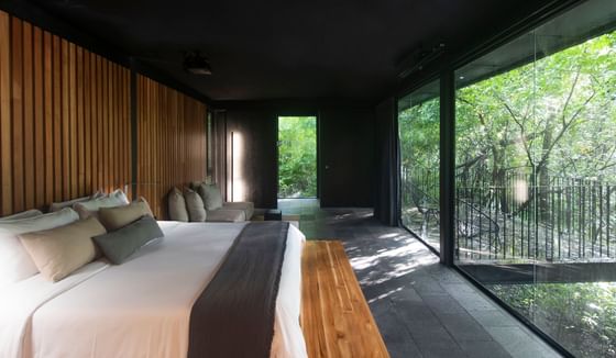 Modern bedroom with large bed and floor-to-ceiling windows overlooking a forest in Center Bungalows at Hotel Rio Perdido