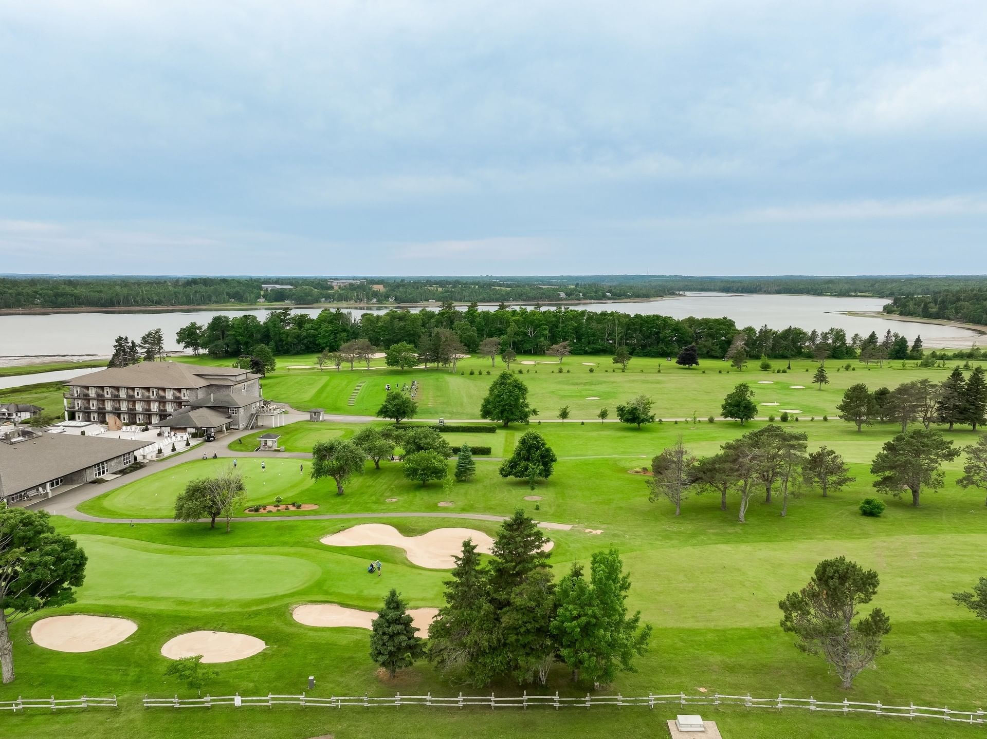 Wide golf course with sand bunkers by a calm river under a cloudy sky at a resort near Rodd Brudenell River Resort