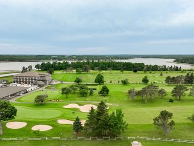 Wide golf course with sand bunkers by a calm river under a cloudy sky at a resort near Rodd Brudenell River Resort