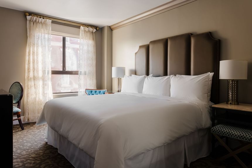 Cozy lounger and nightstand by the bed in Deluxe King Room at Hotel Bijou, offering stylish hotel rooms in San Francisco