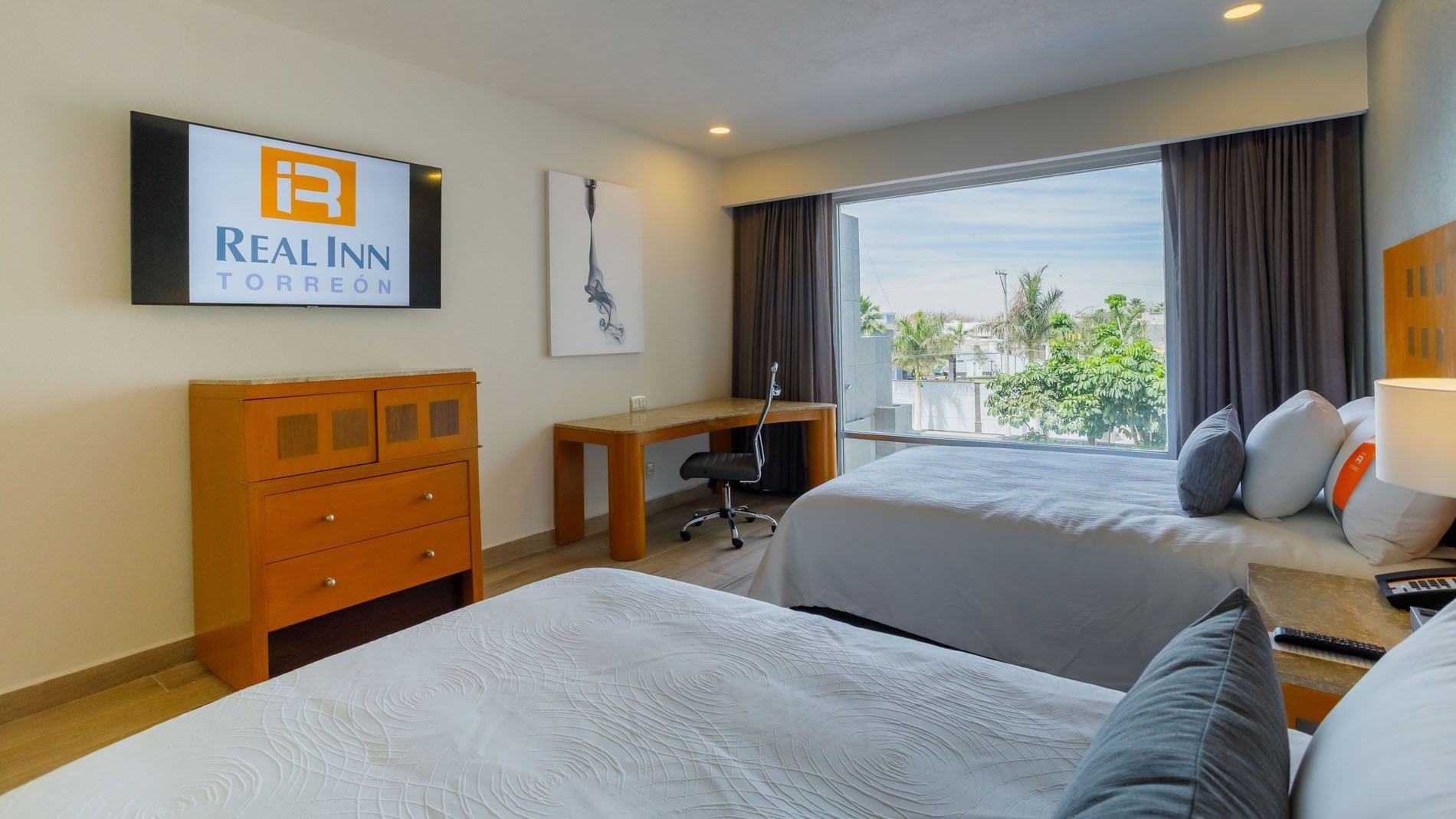 Real Inn Torreon 2 Double Deluxe room with two beds, a large window viewing palm trees, and a branded TV screen