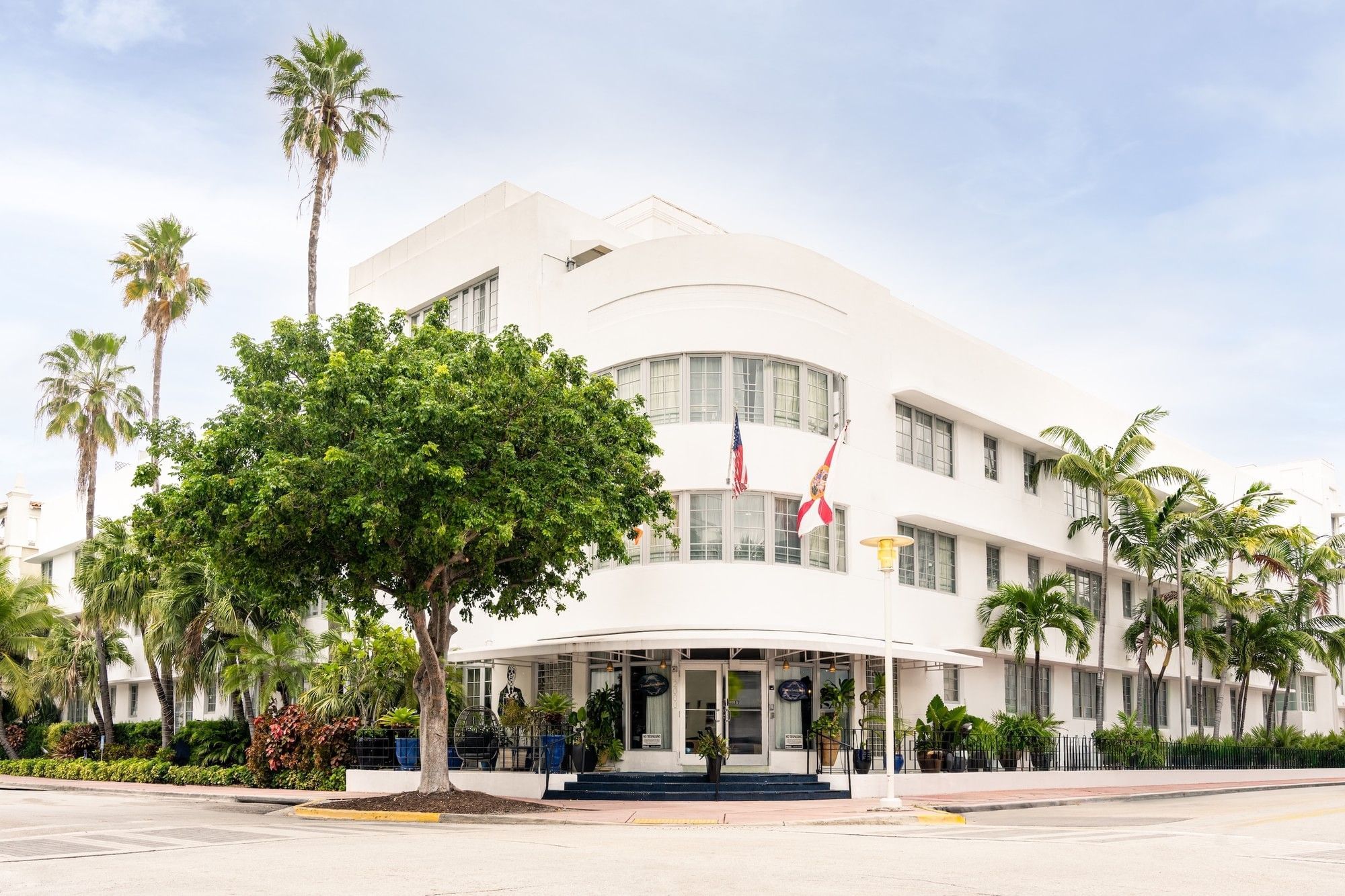A white, multi-story building with a curved front and palm trees in front.