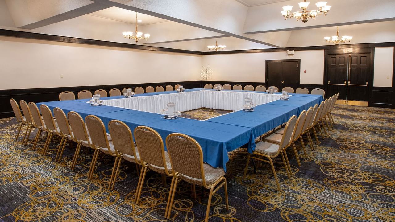 A large conference room with blue tablecloths, chairs, and chandeliers on the ceiling.
