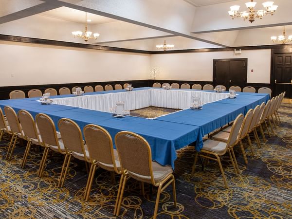 A conference room with a large table covered in blue cloth surrounded by chairs.