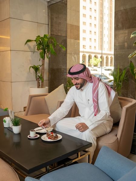 Man in traditional Arab attire enjoying chocolate cake and coffee in Oasis Coffee Shop at Saja Warwick Madinah
