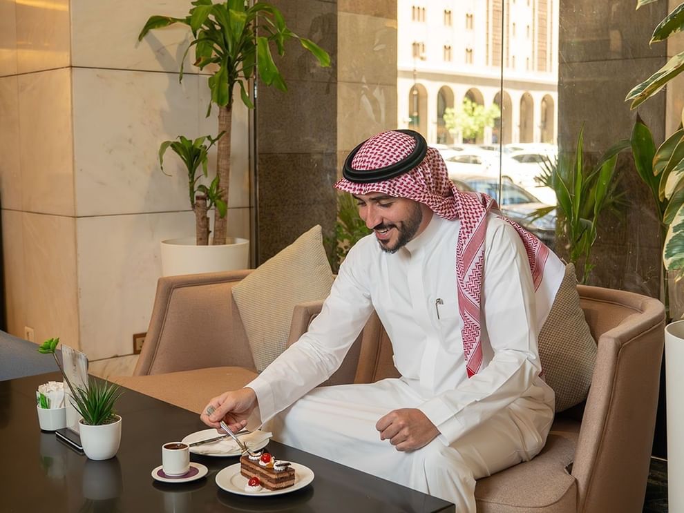 Man in traditional Arab attire enjoying chocolate cake and coffee in Oasis Coffee Shop at Saja Warwick Madinah