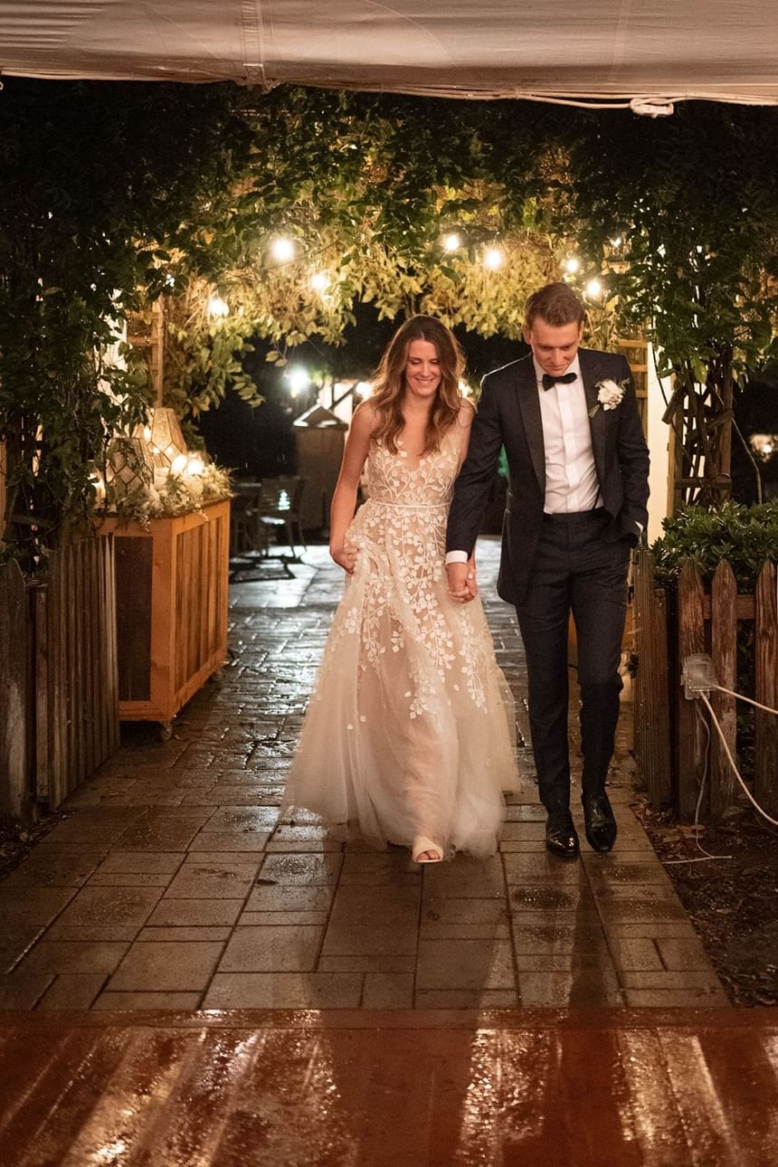 Bride and groom holding hands, walking down a lit outdoor pathway at The Clifton Hotel in Charlottesville, VA.