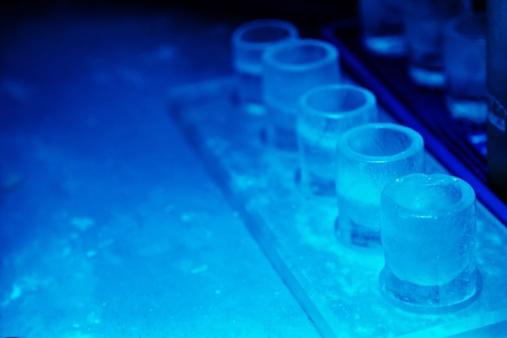 A row of four shot glasses made of ice sit on an icy table. 