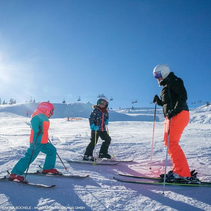 Tre persone sciando su una pista da sci in una giornata di sole.