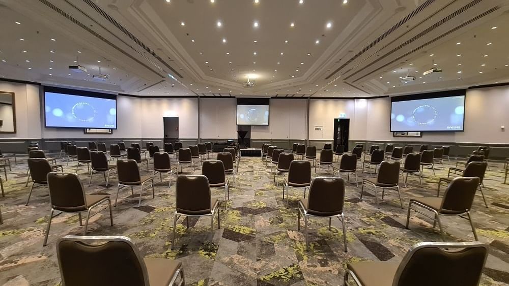 Rows of chairs facing a projector screen under ceiling lighting in Grand Ballroom at Novotel Sydney International Airport 