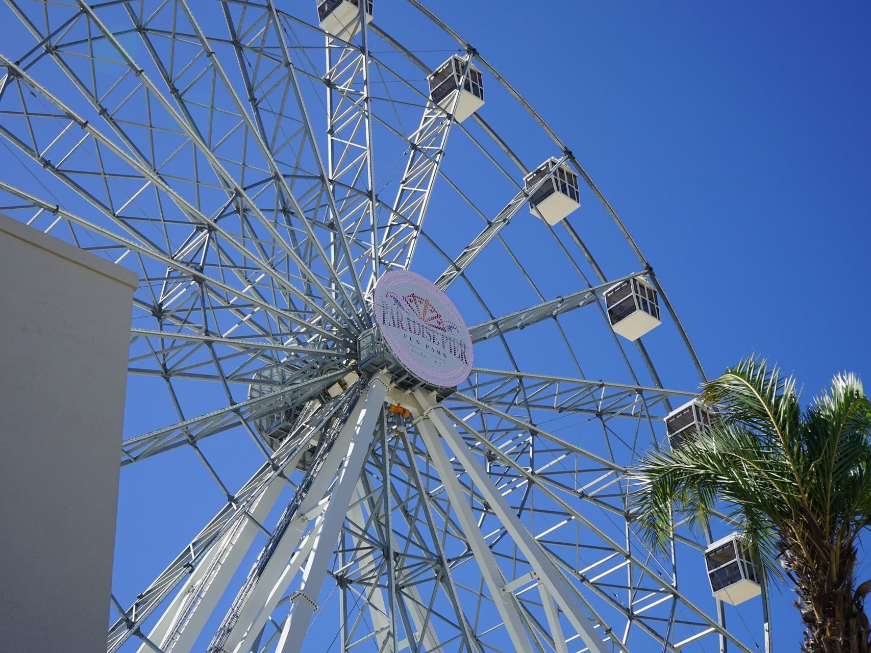 Large Ferris wheel in Paradise Pier Fun Park with white gondolas against a clear blue sky near The White House Hotel