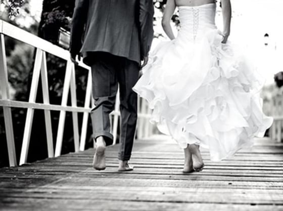 Black & white image of a wedded couple walking on a bridge at Courtleigh Hotel Suites