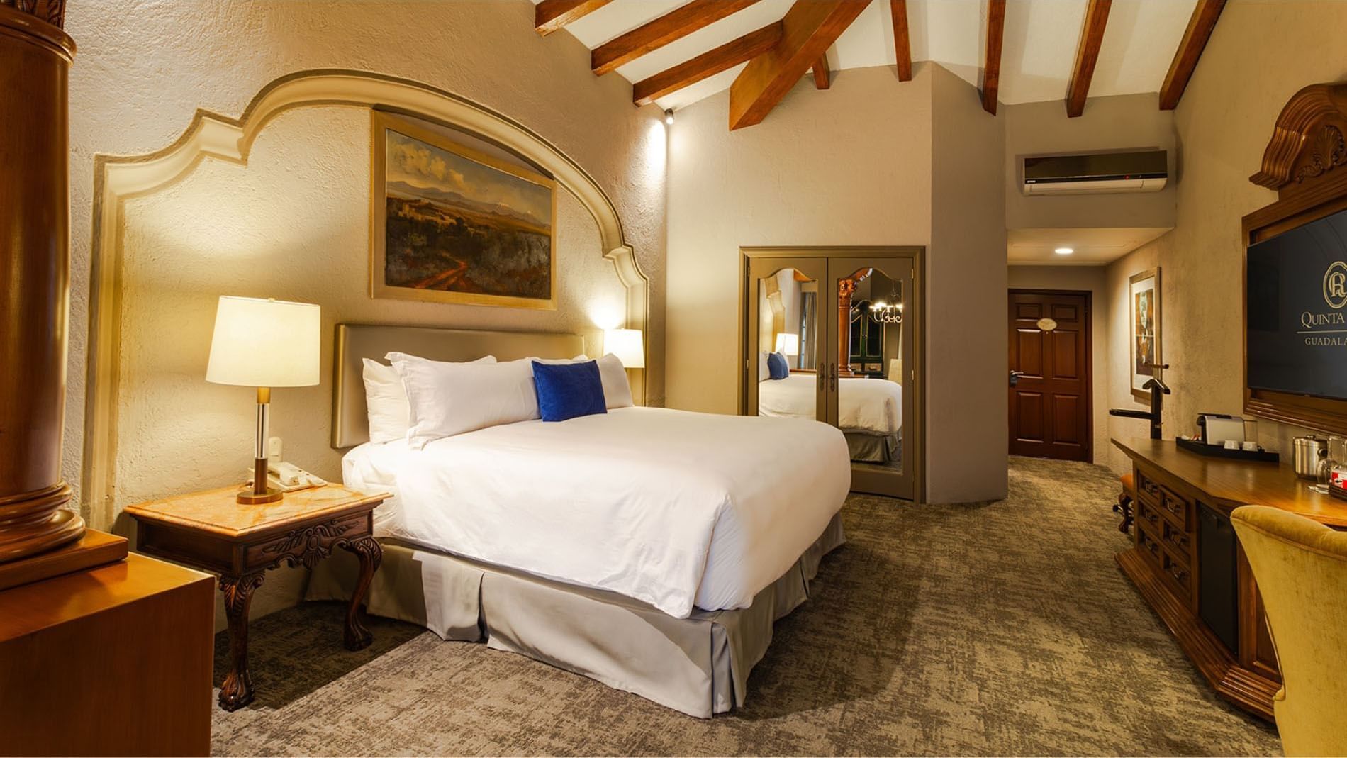 King Grand Class bedroom with vaulted wood beams and a large mirrored wardrobe closet at Quinta Real Guadalajara