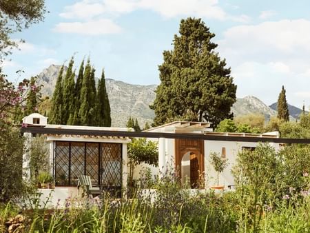 Casa blanca con jardines y montañas al fondo en un día soleado.