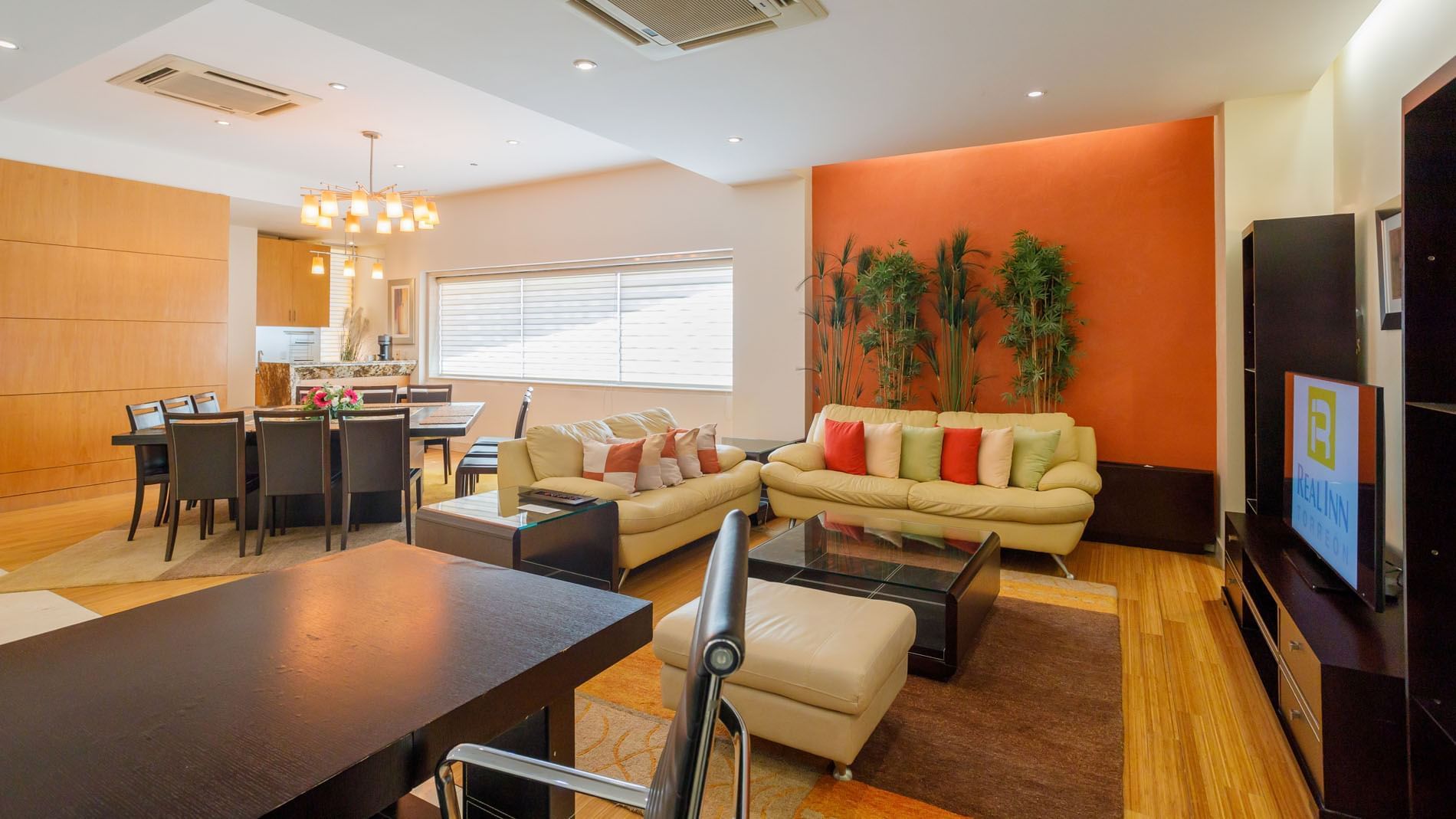 King Presidential Suite living area with a bright orange accent wall, cream sofas, and a dining set at Real Inn Torreon